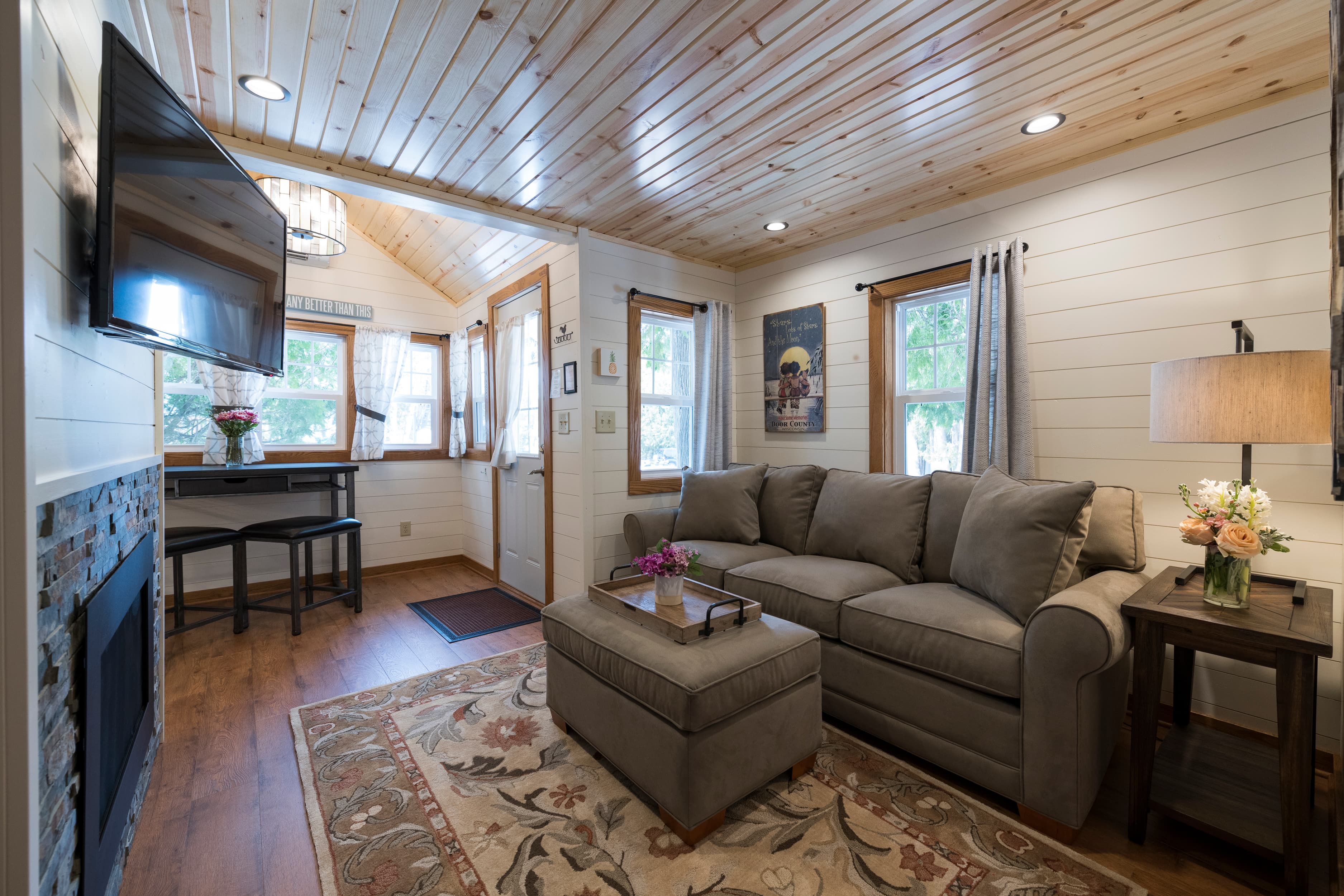 A warm living area with wood-paneled ceilings, a gray sofa, a fireplace, and a dining nook.