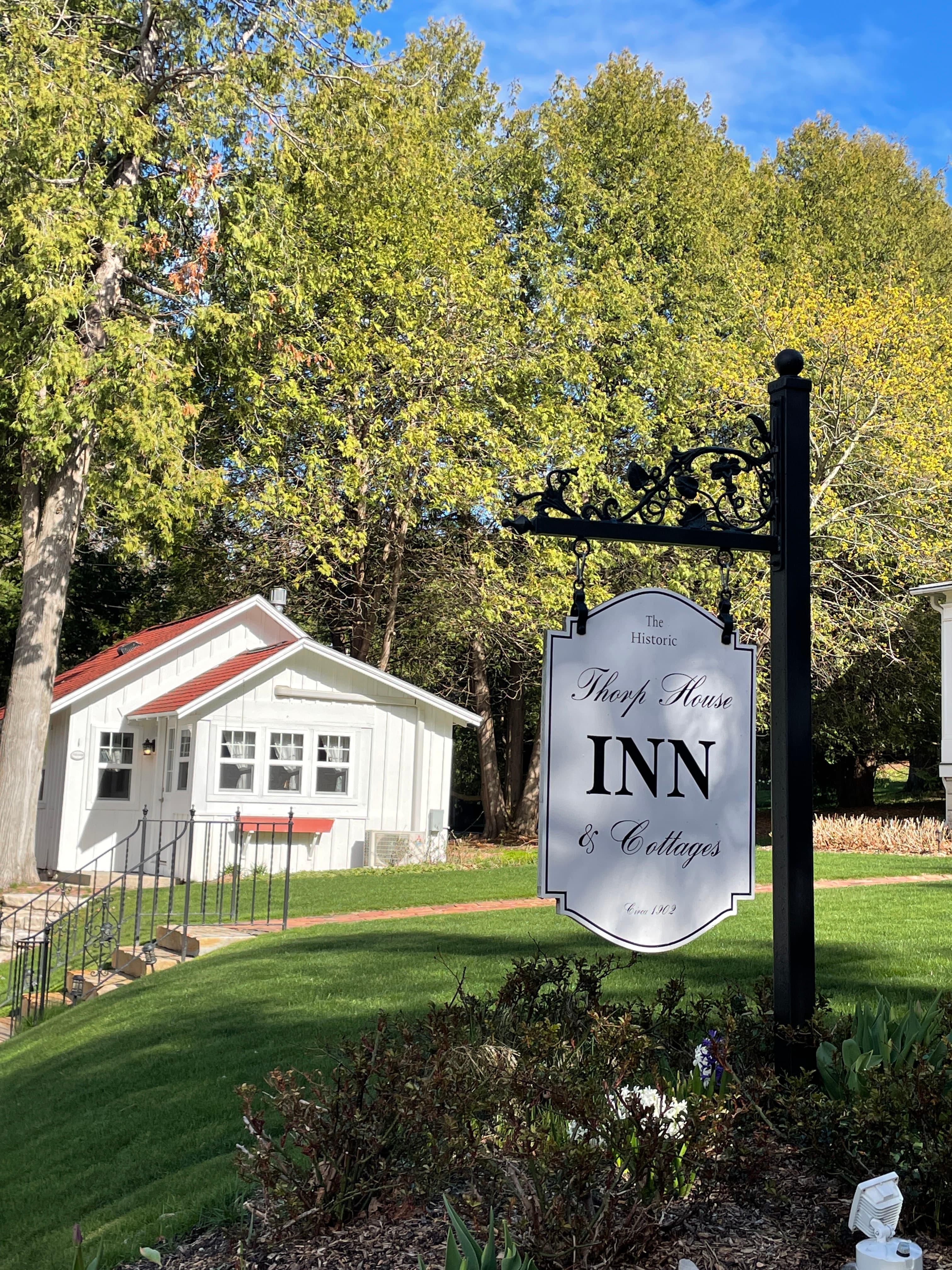 A picturesque view of the inn's sign, with a charming white cottage and lush green trees in the background.