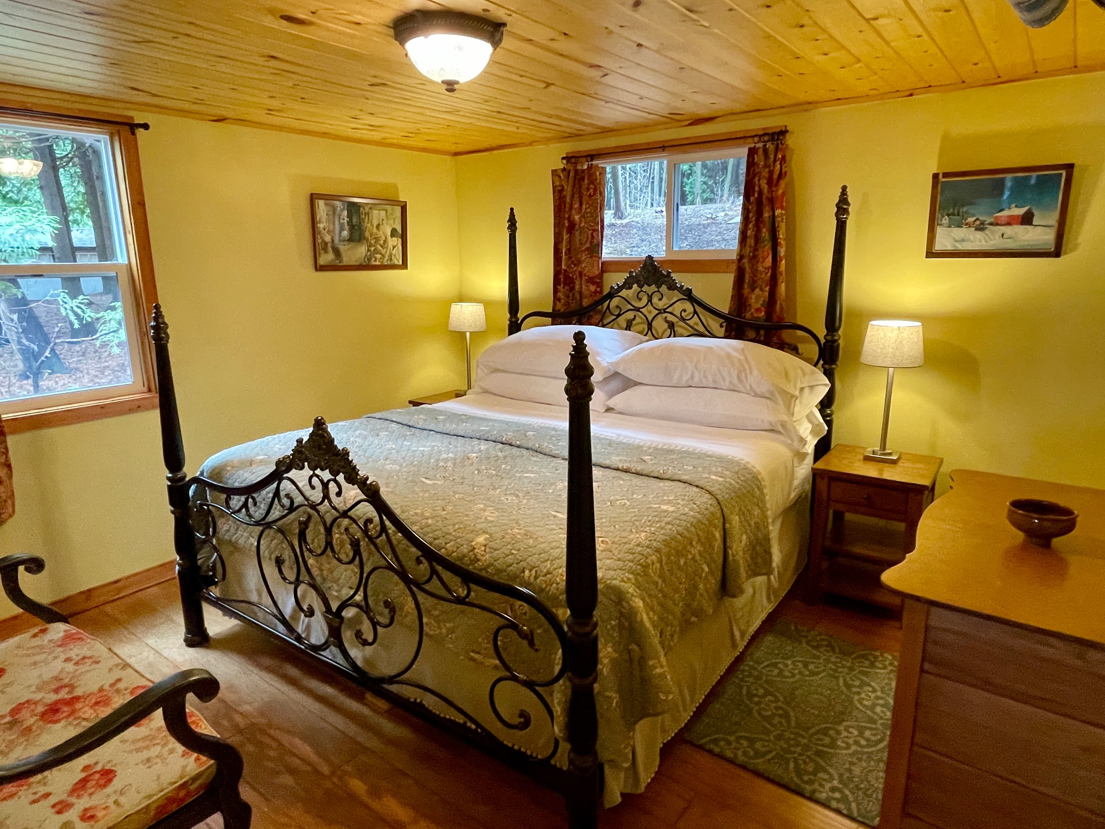 A rustic bedroom featuring a wrought iron four-poster bed, light yellow walls, and wood-paneled ceilings, with cozy lighting.