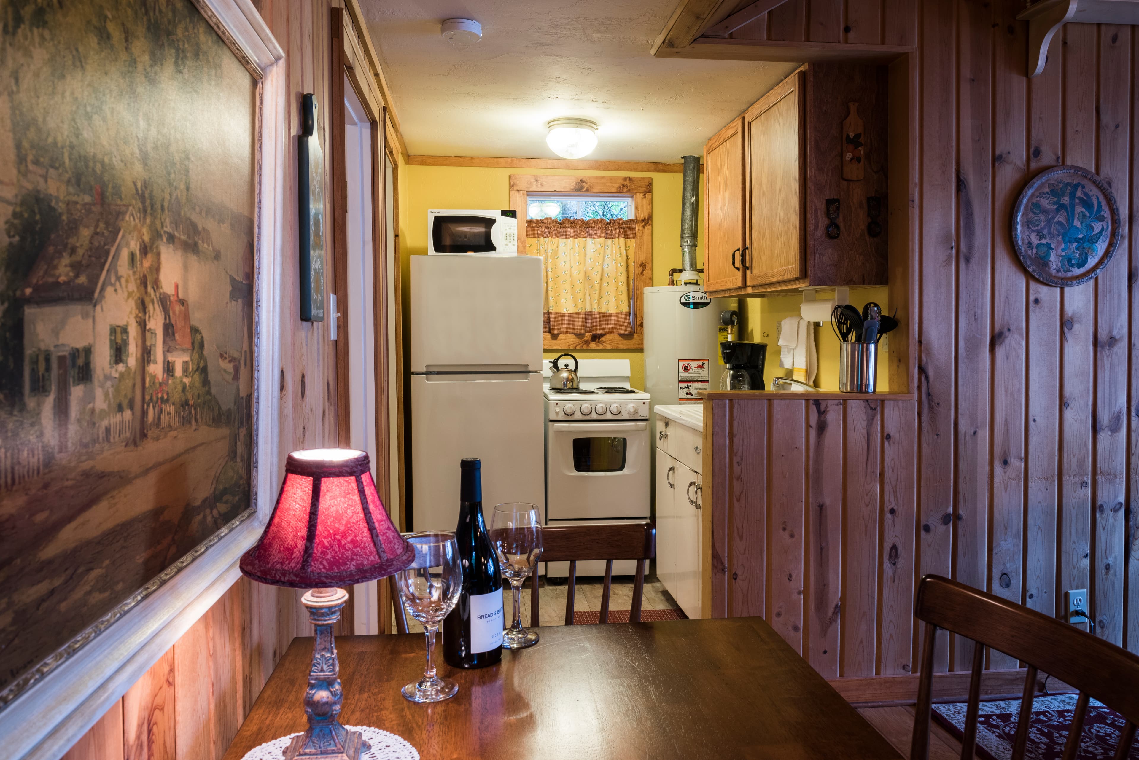 A warm and rustic kitchen and dining area with wood-paneled walls, a small dining table with wine, and a compact kitchen setup.