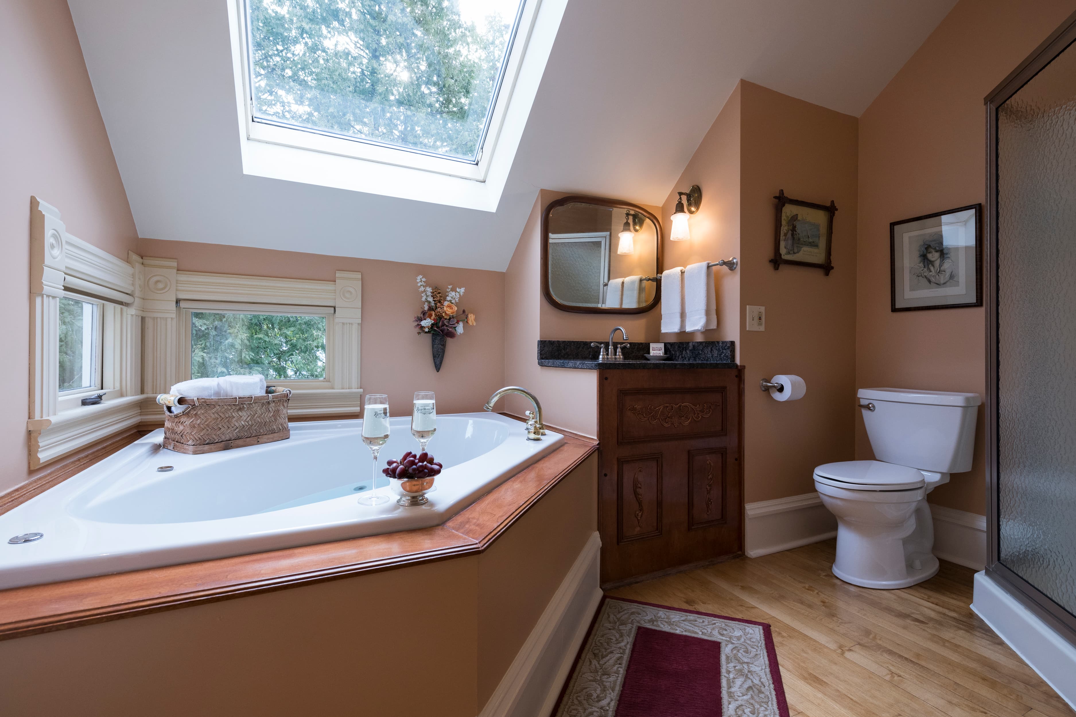 A cozy bathroom featuring a large corner spa tub, a skylight, and a vanity with a mirror, all in warm, inviting tones.