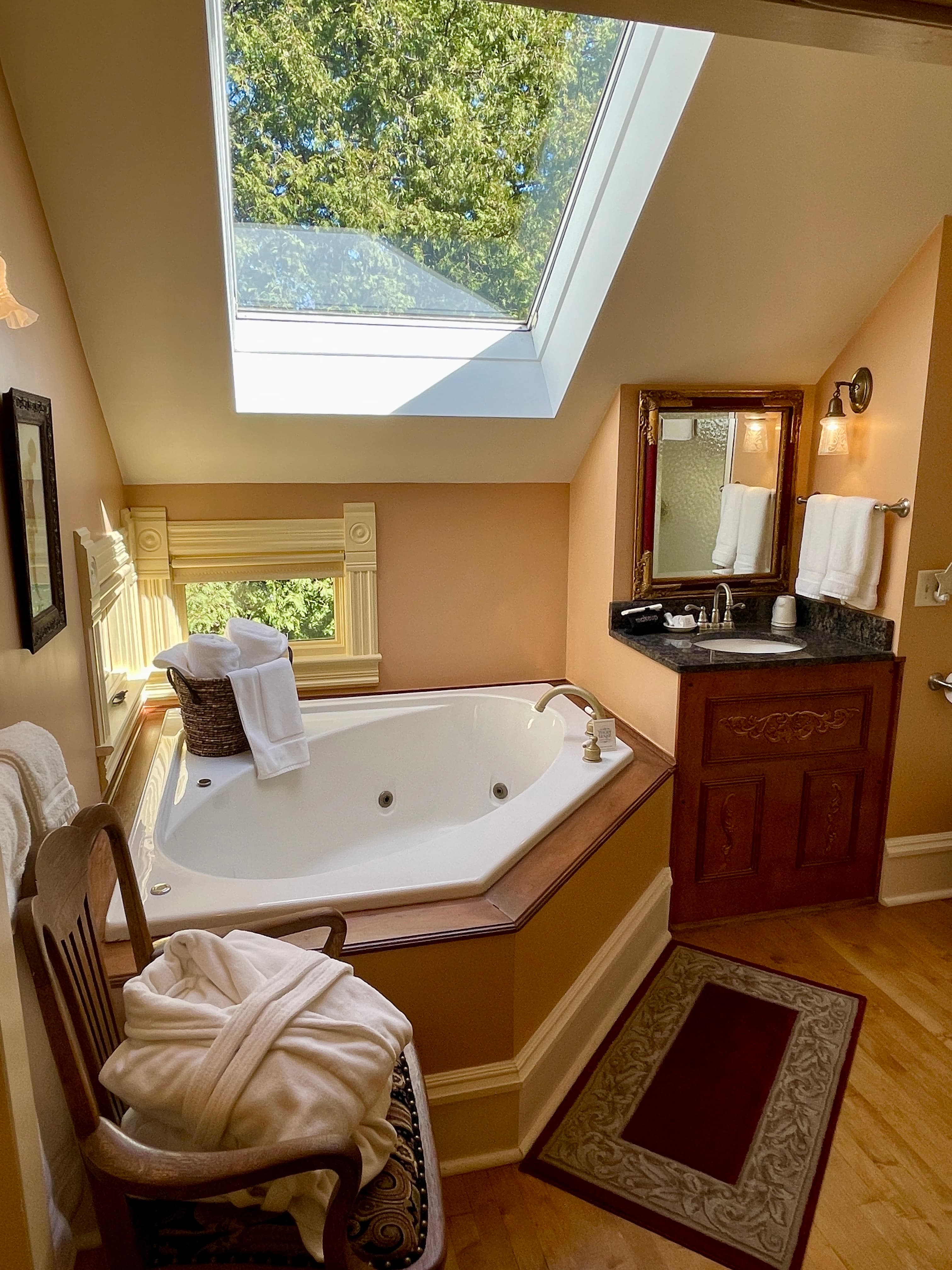 A well-lit bathroom with a large corner spa tub, a skylight, and a wooden vanity, all with a cozy and inviting ambiance.