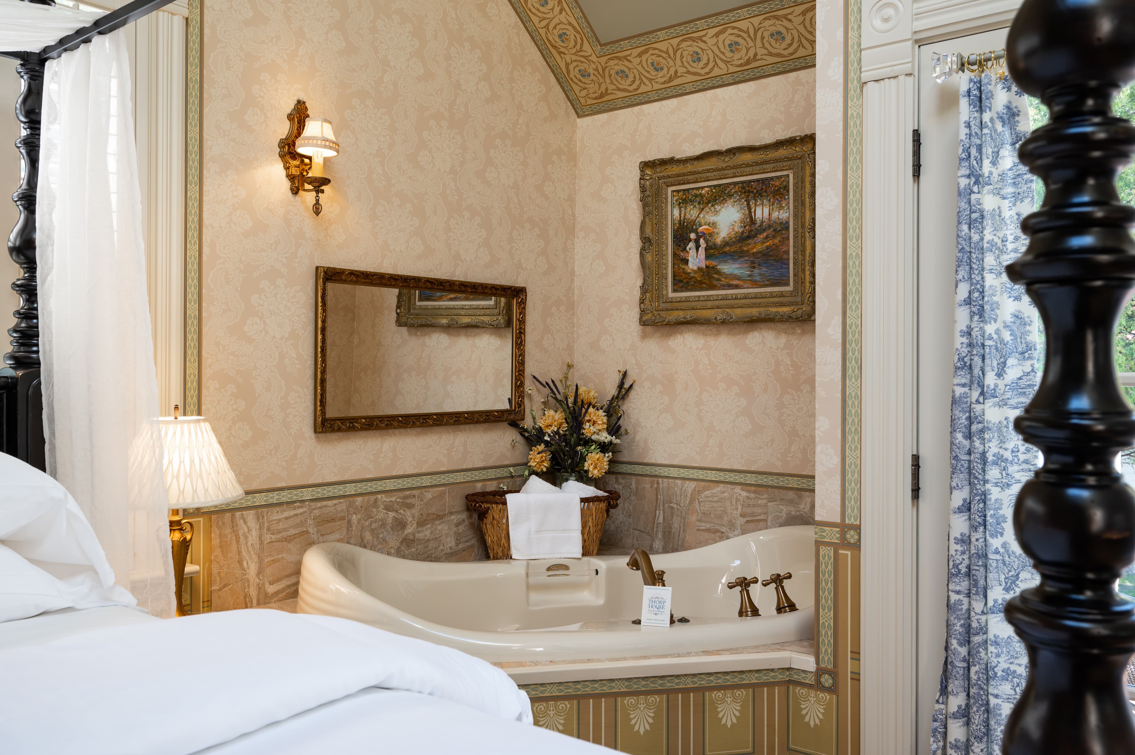 A luxurious bedroom featuring a four-poster bed, an en-suite bathroom with a large soaking tub, and elegant, ornate wallpaper.