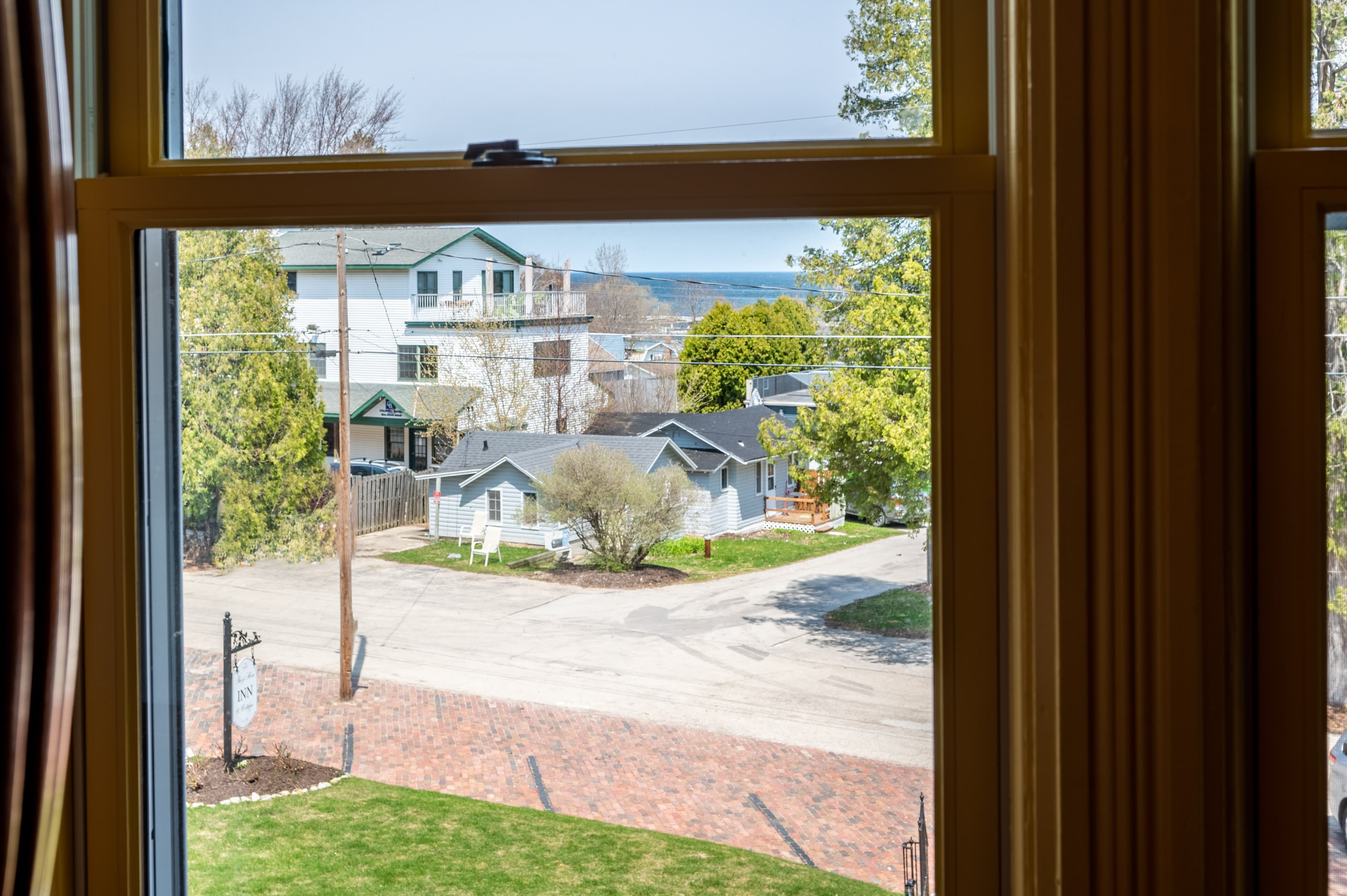 A framed view through a window shows a quiet street with houses, trees, and a glimpse of the harbor in the distance.