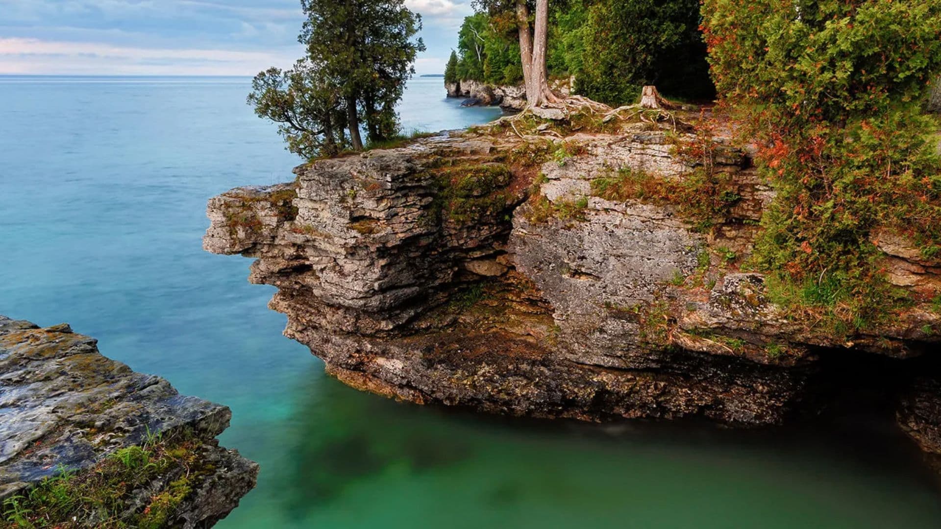 A rocky shoreline meets clear turquoise waters under a bright sky.