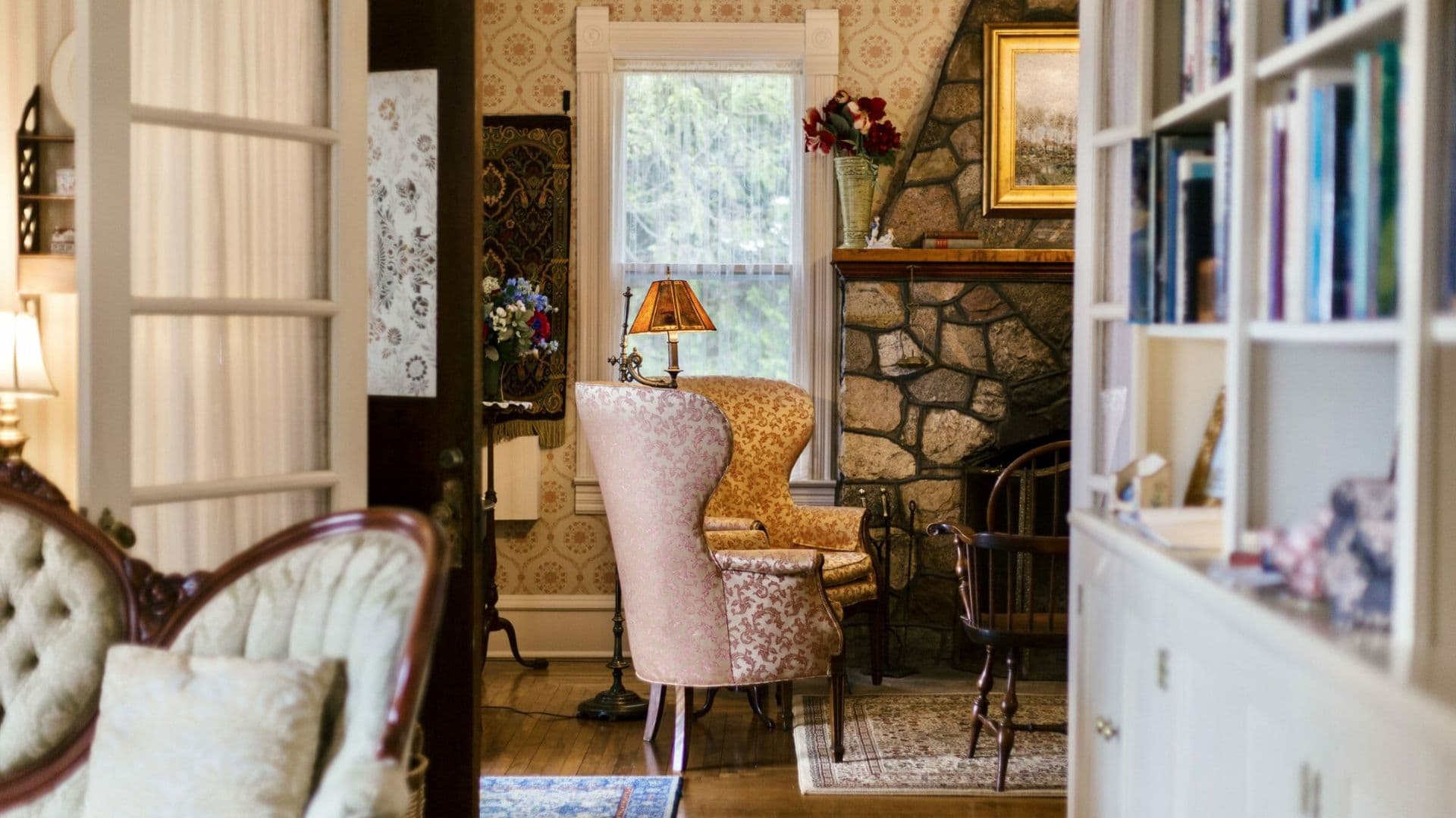 A cozy living room featuring patterned chairs, a stone fireplace, and bookshelves.