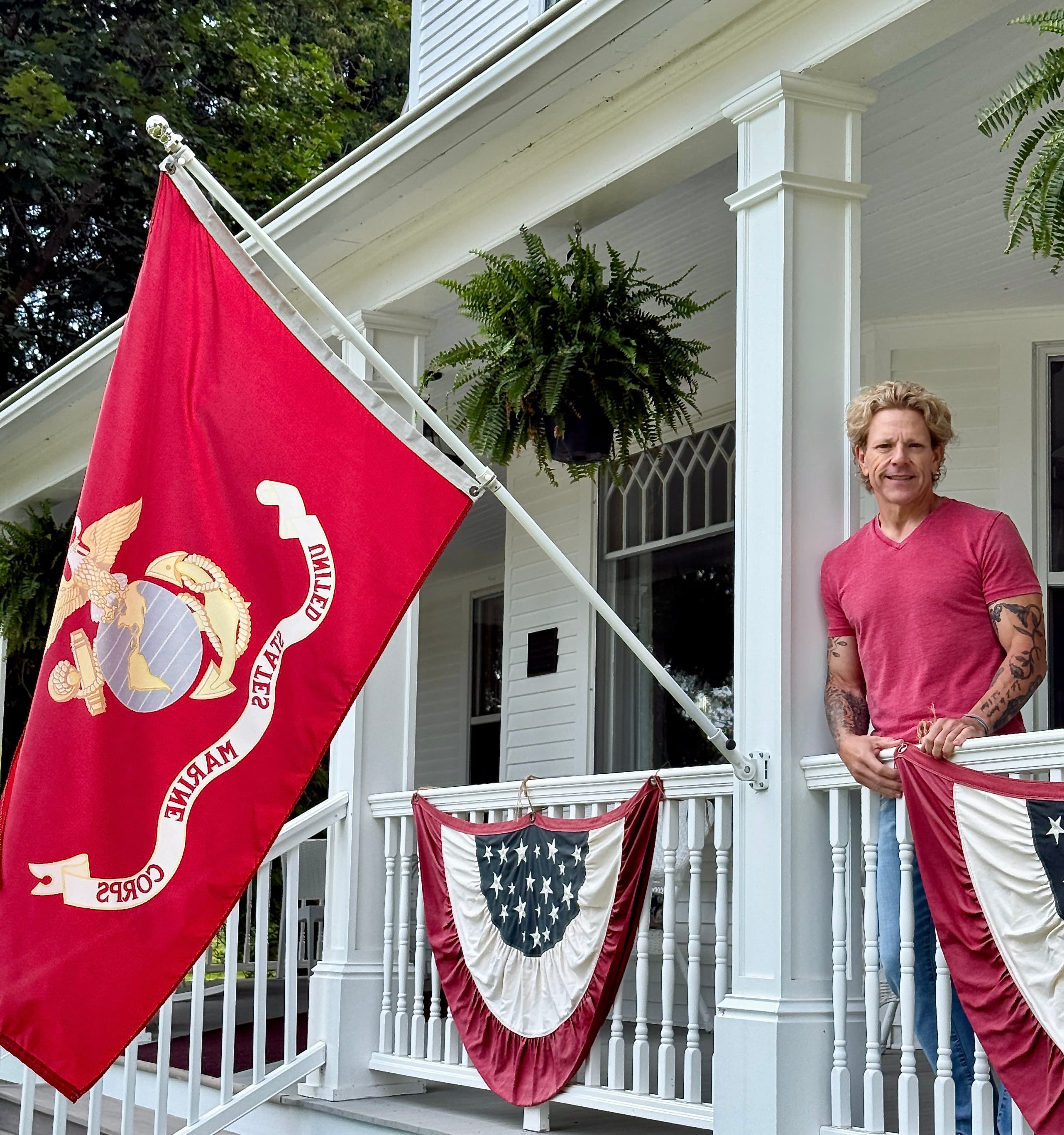 A person stands on a porch decorated with a Marine Corps flag and patriotic bunting.