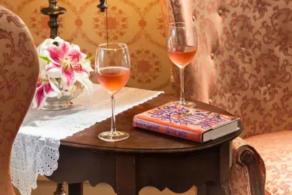 A cozy setting featuring two glasses of rosé wine, a flower vase, and a book on a small table.
