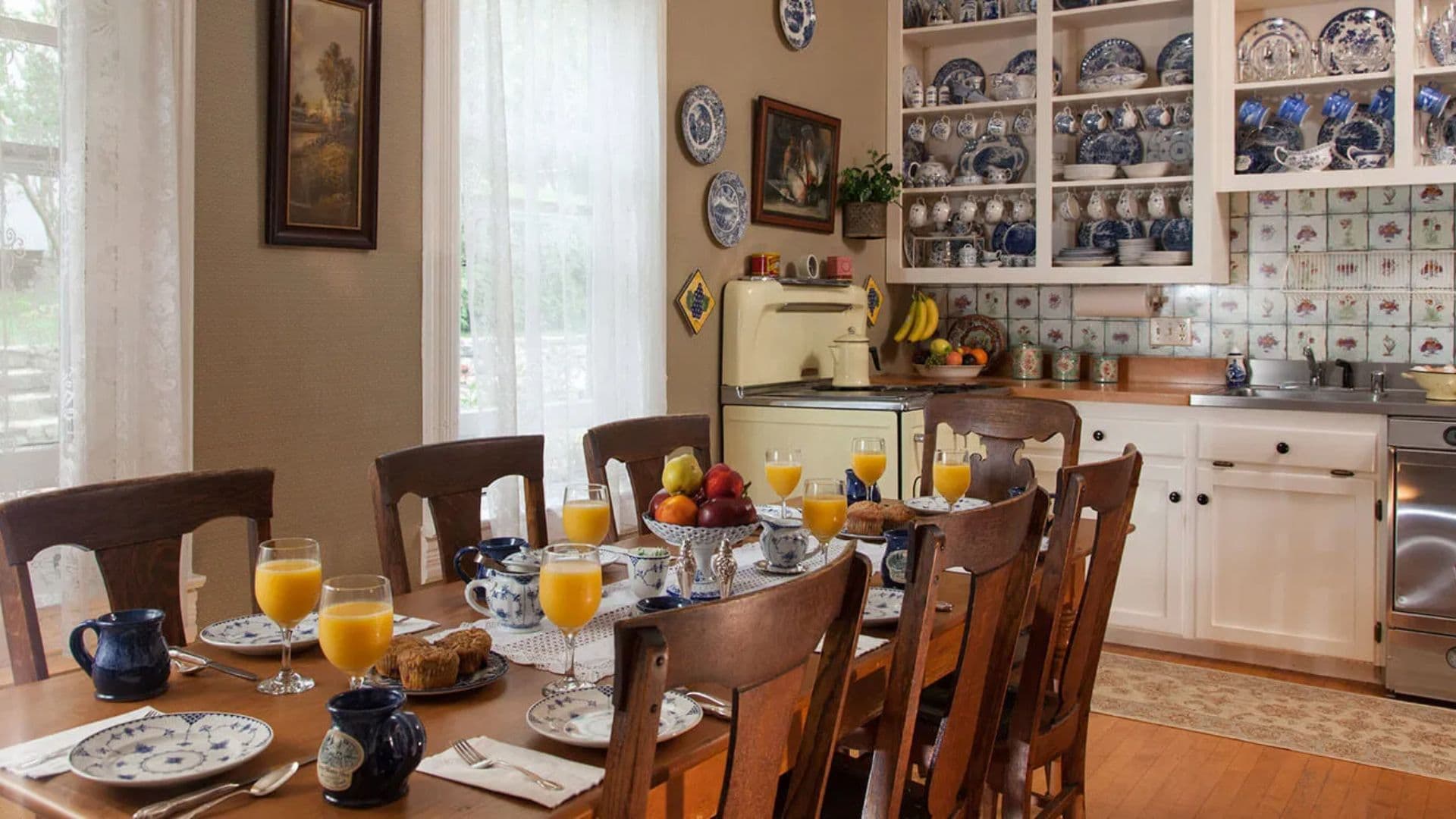 A cozy dining room set for breakfast, featuring a long table with plates, drinks, and fruit, surrounded by charming decor.