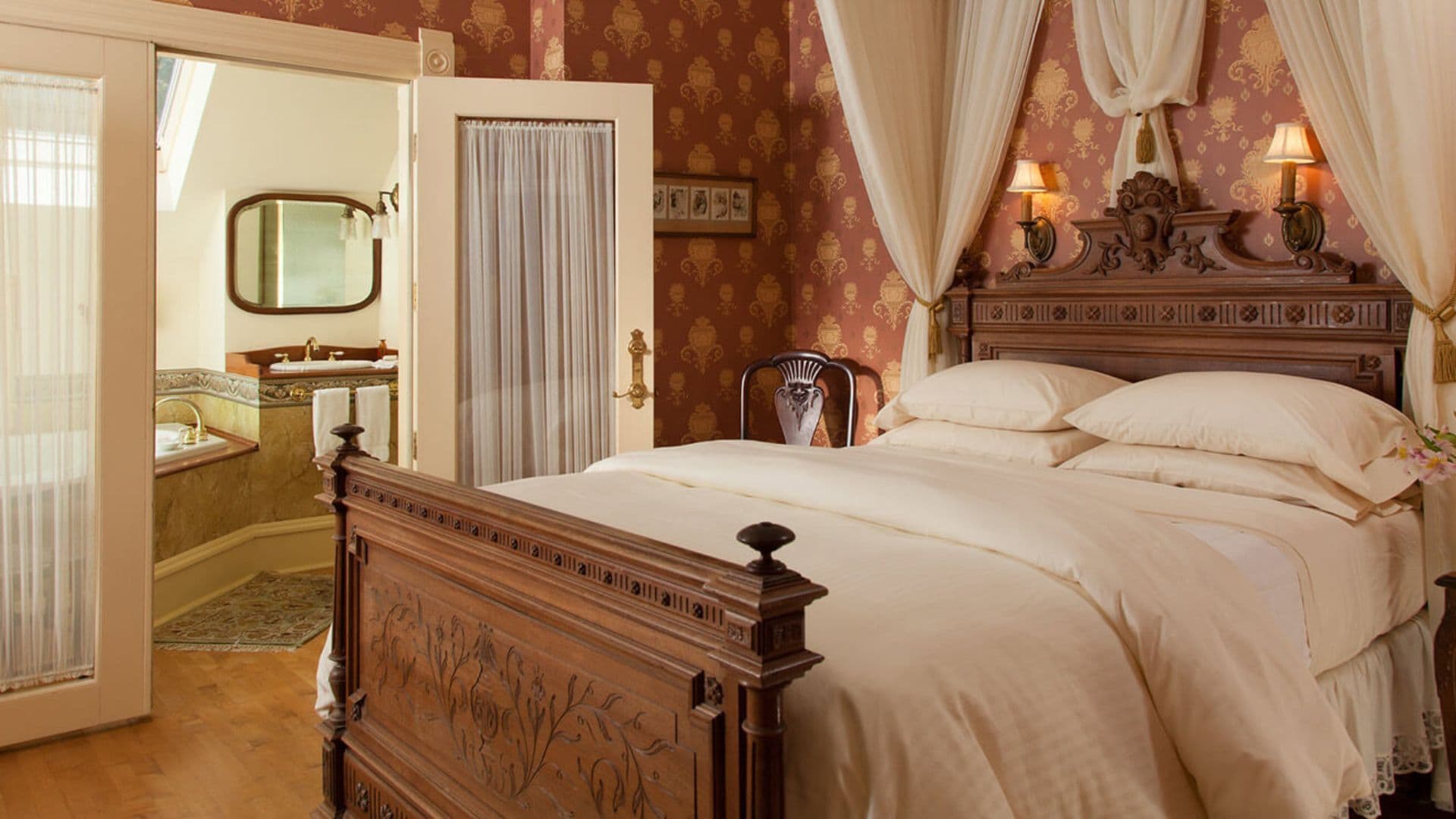 A cozy bedroom featuring a wooden bed with elegant bedding and a view into an adjacent bathroom.