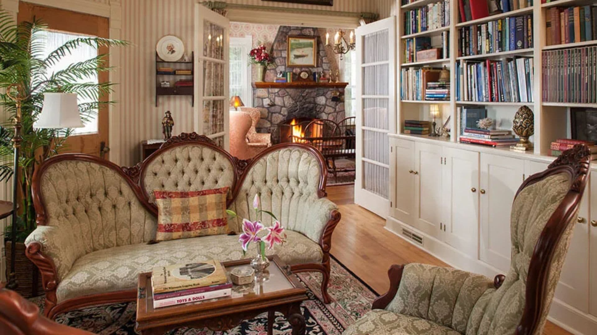 A cozy living room featuring vintage furniture, a fireplace, and a bookshelf.