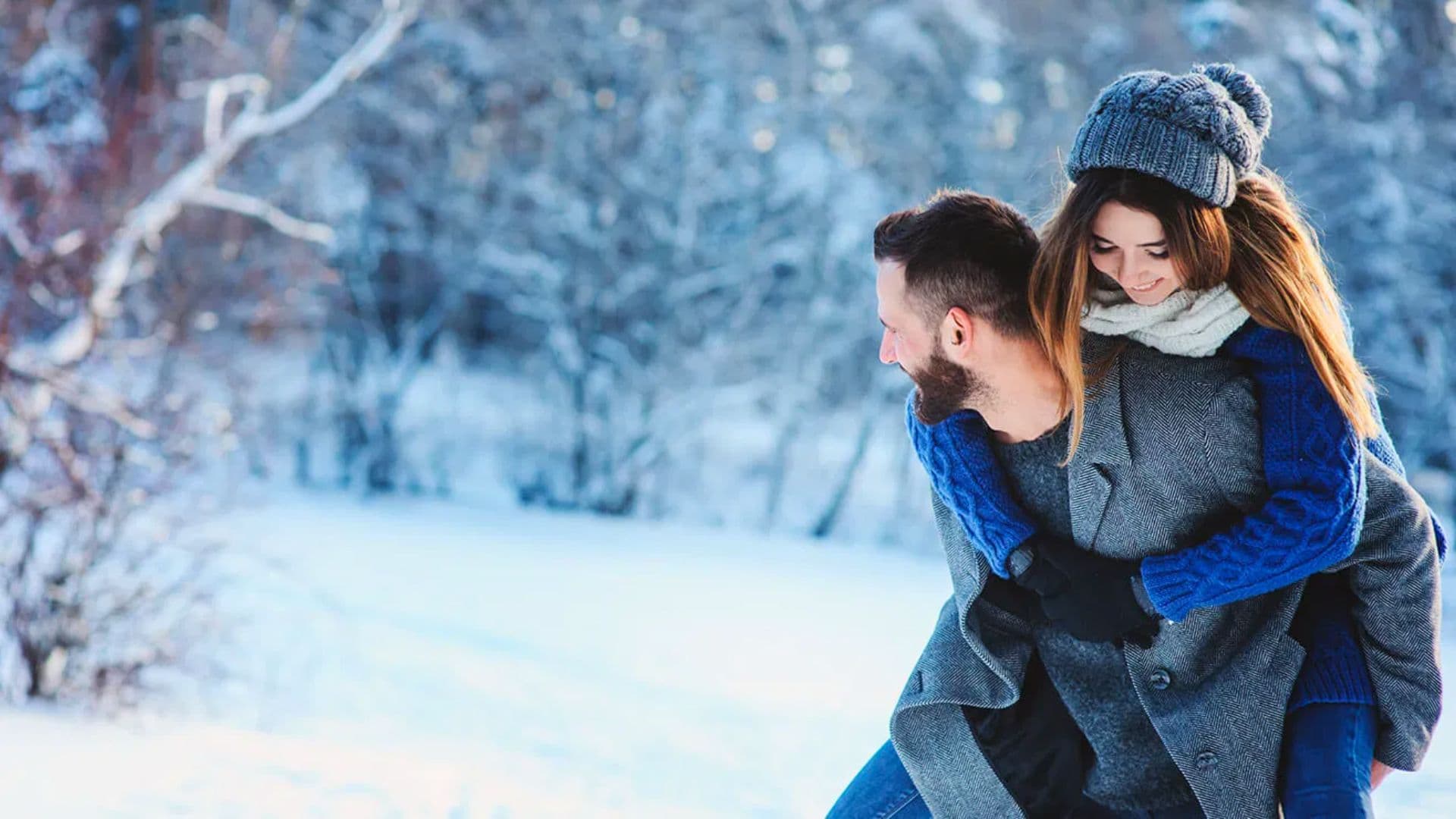 A couple enjoys a playful moment in a snowy landscape, with the woman riding on the man's back.