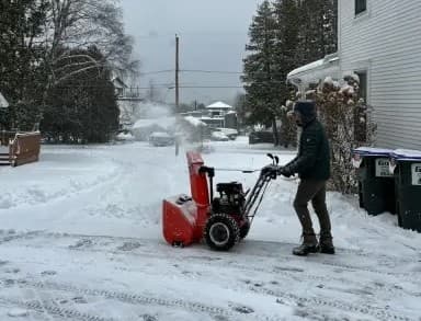 A man snow blowing in a driveway A man snow blowing in a driveway