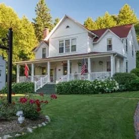 Large white home with red roof with lush grass and surrounded by trees Large white home with red roof with lush grass and surrounded by trees