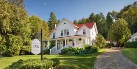Large white home with red roof with lush grass and surrounded by trees Large white home with red roof with lush grass and surrounded by trees